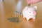 Selective focus of Men hand putting coin to piggy bank with stack of coin on wooden desk fill with natural light background.