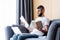 Selective focus of pensive freelancer holding notebook and book near laptop and medical mask on sofa