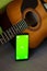 Selective focus on phone with greenscreen of chromakey mockup with tracking markers near the guitar with copy space. Green screen