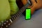 Selective focus on phone with greenscreen of chromakey mockup with tracking markers near the guitar with copy space. Green screen