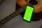 Selective focus on phone with greenscreen of chromakey mockup with tracking markers near the guitar with copy space. Green screen