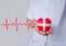 Selective focus of red heart wrapped by white plus sign bandages as a gift with red line of cardiogram. The heart holded by doctor