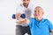 selective focus of rehabilitation therapist assisting senior man exercising with dumbbell