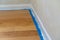 Selective focus on section of blue painters tape next to wall trim and hardwood floors, during a home renovation and painting