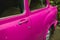 Selective focus shot on the side doors of a pink retro car standing in front of green plants