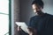 Selective focus.Smiling bearded African man reading news digital tablet while standing near the window in his modern