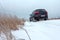 Selective focus. SUV car racing on snowy road in countryside during winter travel. Track of vehicle in snow