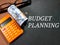 Selective focus.Text BUDGET PLANNING on a black background with money,calculator and glasses.Business concept idea.