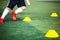 Selective focus to cone marker with blurry boy soccer player is jogging on green artificial turf