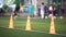 Selective focus to orange marker cone is soccer training equipment on green artificial turf with blurry coach and kid soccer