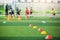 Selective focus to red and yellow marker cones are soccer training equipment on green artificial turf with blurry kid players trai