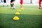 selective focus to yellow cone marker is soccer training equipment on green artificial turf with blurry kid players training