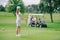 selective focus of woman with golf club looking at friends resting at golf cart