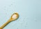 Selective focus on wooden spoon with small white round homeopathy pills against blue background.