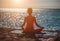 Selective focus. Young beautiful caucasian woman in a red suit practicing yoga on the beach at sunrise near the sea