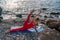 Selective focus. Young beautiful caucasian woman in a red suit practicing yoga, fitness and stretching on the beach at