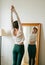 Selective focus young woman doing morning stretch in front of mirror in bedroom. Women`s health and wellbeing. Good morning