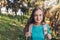 Self-confidence. Teenage girl looking at camera carrying backpack with serene smile in forest.