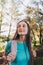 Self-confidence. Young woman with turquoise t-shirt, carrying backpack with serene smile in forest. Vertical