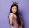 Self-confident asian kid girl princess in party dress and with a painted red hearts sign on cheeks makes force gesture