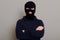 Self-confident criminal male posing isolated on a gray background, wearing a black hoodie and a bandit mask, looking at the camera