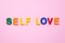 Self love text on pink paper background made from colorful plastic letters. Multicolored inscription on the banner. Title,