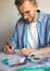 A self-taught seamster with glasses is working at the table. A DIY designer draws a sketch for a new costume project. A smiling