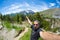 Selfie of adult hiker on top of trail crossing high altitude conifer woodland with snowcapped mountain range in background and moo