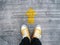 Selfie feet wearing yellow sneakers in front of arrow on concrete road