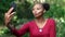 Selfie, kiss or happy black woman in park with nature, smile and happiness by trees. Girl and female with smartphone for