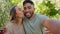 Selfie, love and interracial couple in park kiss for bonding, quality time and relax on weekend date. Nature, dating and