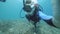 Selfie portrait video of a male scuba diver swimming underwater at the ocean floor.