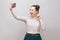 Selfie time! Portrait of happy foolish joyful attractive blogger woman wearing in striped shirt standing, winking and showing