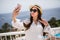 Selfie time. Young lady in summer hat and sunglasses, having lunch on a summer open air light terrace outdoors at sea background