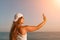 Selfie woman sea. The picture depicts a woman in a cap and tank top, taking a selfie shot with her mobile phone