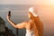 Selfie woman sea. The picture depicts a woman in a cap and tank top, taking a selfie shot with her mobile phone