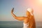 Selfie woman sea. The picture depicts a woman in a cap and tank top, taking a selfie shot with her mobile phone