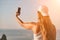 Selfie woman sea. The picture depicts a woman in a cap and tank top, taking a selfie shot with her mobile phone