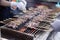 Seller grilling tasty bbq meat with wooden skewers on fire