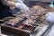 Seller grilling tasty bbq meat with wooden skewers on fire