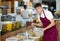 Seller guy in supermarket scooping marinated green olives