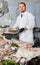 Seller holds basket of small mussels standing near a counter