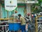 a seller of indonesian snack called pentol with a green shirt and a blue cart seen from behind