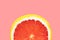 Semi circle slice of ripe juicy red grapefruit on cherry pink background. Citrus fruits summer vitamins