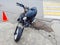 A semi-disassembled moped with wires sticking out is parked on the side of a road with broken asphalt