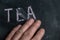 The semi-erased word TEA on the black chalkboard. An adult man`s left hand removes the handwritten word with his fingers. Fuzzy