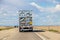 Semi tractor trailer truck on desert highway with shiny back reflecting sky and pavement in blurry pattern - more trucks and
