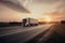 A semi truck driving down a long, empty highway at sunset