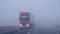 A semi truck jackknifed on a highway partially hidden in a dense fog