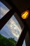 Semicircular wooden window overlooking  blue cloudy sky, with incandescent bulb on background